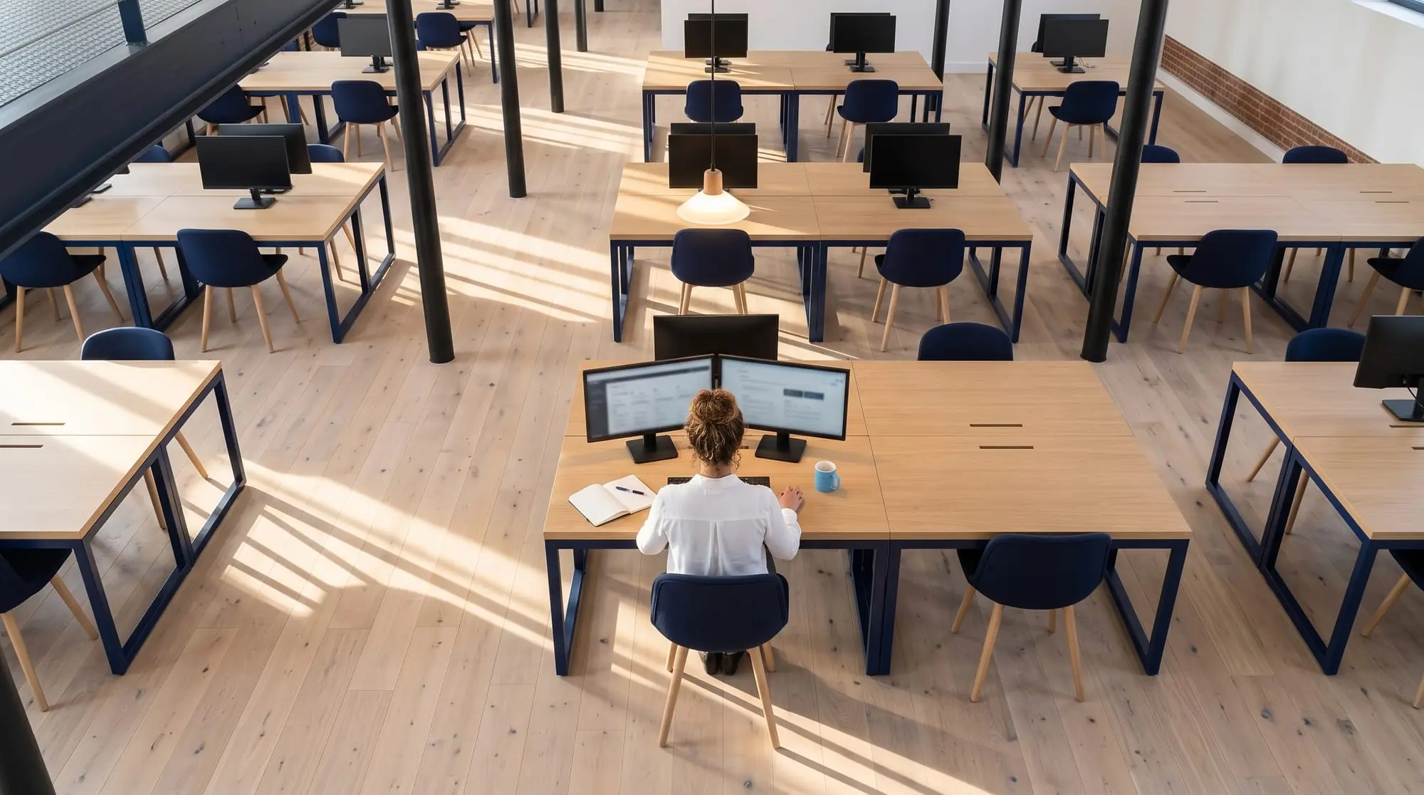 Illustration générée par intelligence artificielle : vue plongeante sur un plateau de bureaux désert, une seule personne encore à son poste sous une suspension allumée